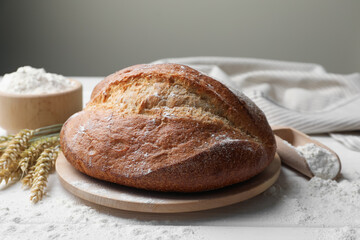 Loaf of fresh bread, flour and spikes on white wooden table, closeup