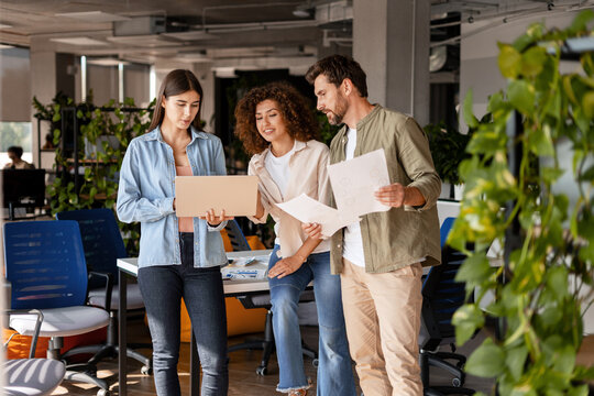Marketing team working together analyzing strategy on laptop and documents