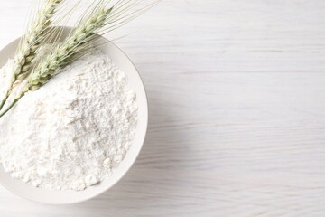 Green wheat spikes and flour on light wooden table, top view. Space for text
