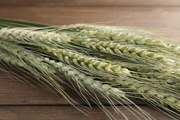 Many green wheat spikes on wooden table, closeup