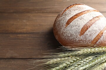 Fresh bread and green wheat spikes on wooden table, closeup. Space for text