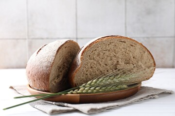 Pieces of fresh bread and green wheat spikes on white wooden table, closeup