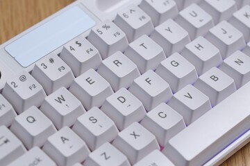 Modern white keyboard with RGB lighting on wooden table, closeup