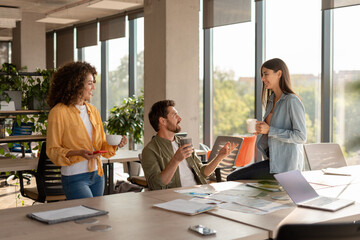 Coworkers enjoying coffee break and discussing project in modern office