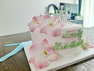 Fresh whipped cream cake decorated with real pink floral petals, edible white pearls and small Tiara on the home table - closeup	