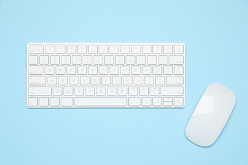 Modern white wireless keyboard and mouse on light blue background, top view