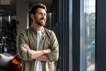 Confident businessman smiling and looking out the window in modern office