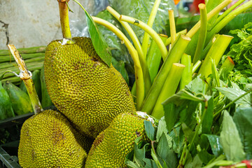 Fresh tropical jackfruit and green vegetables displayed for sale at a local market in Phuket,...