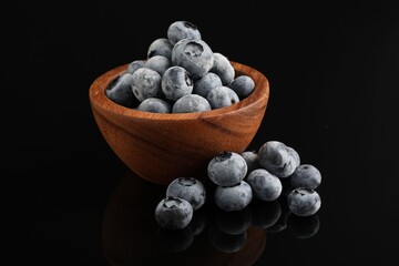 Many frozen blueberries in bowl on black table, closeup