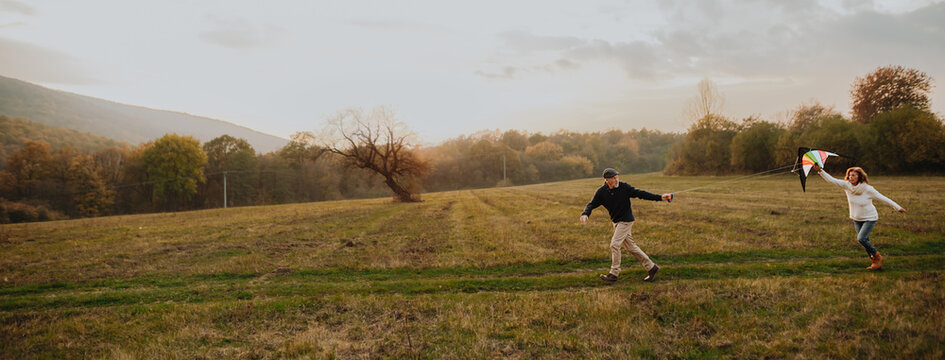 Senior couple flying a kite during warm autumn evening.