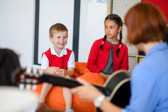 School kids and teacher with guitar sitting in circle on floor. Morning Circle.