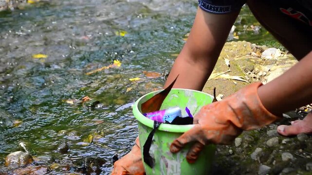 Close-up photo of volunteers sitting and picking up trash in the river. Sanitation workers collect trash in the dirty river into trash buckets. Volunteers clean the river. Environmental care, 