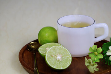 A hot pale yellow tea in a white pearl cup sits on a wooden tray, with a half lemon placed beside it.


