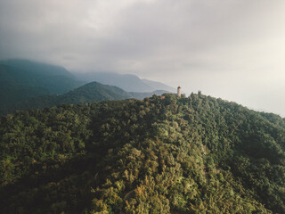 aerial view of a lush, forested mountain range under a cloudy, overcast sky. A small pagoda sits...