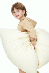 Boy holding a large fluffy pillow, light background.