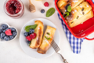 Traditional German  Pfannkuchen-Auflauf, baked pancakes casserole. Sweet dessert casserole for breakfast made with thin pancake crepes with cream cheese, with fresh berry and powdered sugar