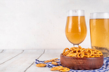Oktoberfest greeting card background with two beer glasses, salted snack and pretzels. Oktoberfest bar, cafes menu on white wooden table, with checkered napkin and decor in Oktoberfest holiday style