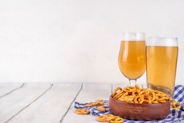 Oktoberfest greeting card background with two beer glasses, salted snack and pretzels. Oktoberfest bar, cafes menu on white wooden table, with checkered napkin and decor in Oktoberfest holiday style