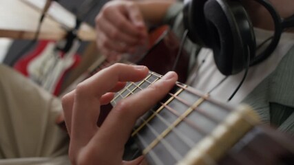 Close-up rack focus view of unrecognisable young man wearing black headphones around neck playing acoustic guitar - Powered by Adobe