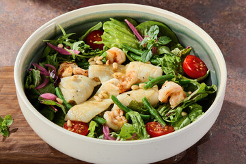 Green salad with squid and shrimp in bright overhead composition with rustic tabletop