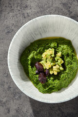 Avocado spinach spread in ceramic bowl, bright natural light, overhead composition with rustic stone background
