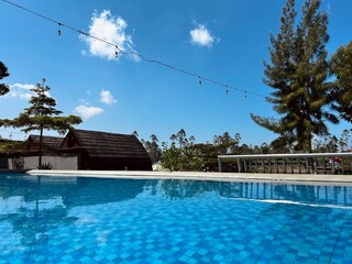A serene outdoor swimming pool with vibrant blue tiles and a reflection of the rustic cabins and...
