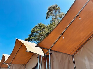 A low-angle view of the repeating canvas roofs of luxury glamping tents, showing their modern...