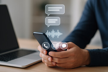 Mobile phone with communication icons and hands holding device near laptop