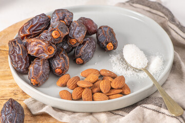 Medjool dates and almonds on a plate with a spoonful of shredded coconut, set on a wooden board with a jar of dates in the background