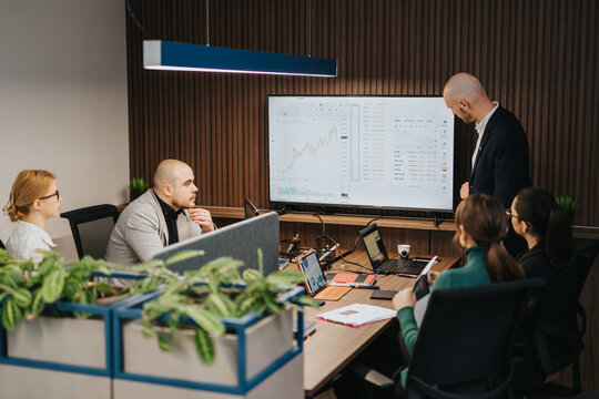 Group of colleagues analyzing data on a large monitor, collaborating and discussing business trends in an office.