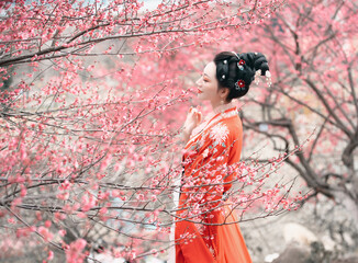 Woman in traditional attire amidst pink blossom trees.