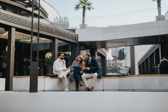 People engage in a discussion while working together on a laptop outdoors, emphasizing teamwork and collaboration in a professional setting, surrounded by modern architecture and natural elements.