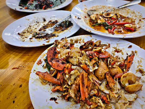 The messy remains of seafood on a large white plate in the foreground contain the remains of empty crab shells and claws. - Powered by Adobe