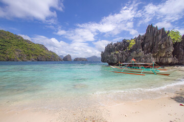 Tropical beach with turquoise waters and traditional outrigger boat in the Philippines