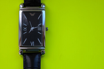 A saturated lime green background highlights the clean lines and geometric design of a rectangular wristwatch. This minimalist image is perfect for illustrating precision, style, and control over time