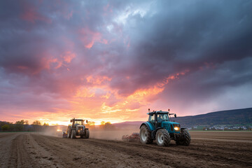 Tractors plowing harvested field under dramatic sunset sky, 
