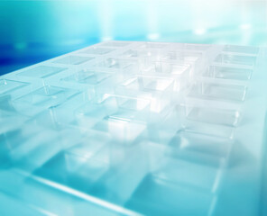 An industrial transparent square thermoforming mold made of plastic as a packaging solution for industrial products. Foil cubes on a blue background and shining lights.	