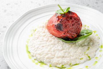 Stuffed roasted red bell pepper on creamy risotto, garnished with spinach and herb oil, served...