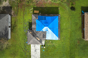 Aerial view of damaged in hurricane Ian house roof covered with blue protective tarp against rain...