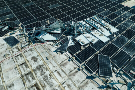 Aerial view of damaged by hurricane wind photovoltaic solar panels mounted on industrial building roof for producing green ecological electricity. Consequences of natural disaster