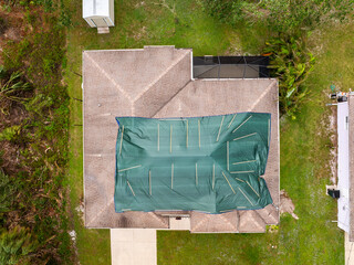 Top view of leaking house roof covered with protective tarp sheets against rain water leaks until...