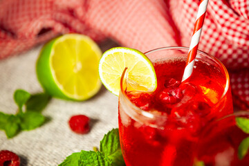 Minimal close-up of red drink with ice, lime and berries. Simple cocktail presentation with fruit and natural garnish — quiet and focused composition.
