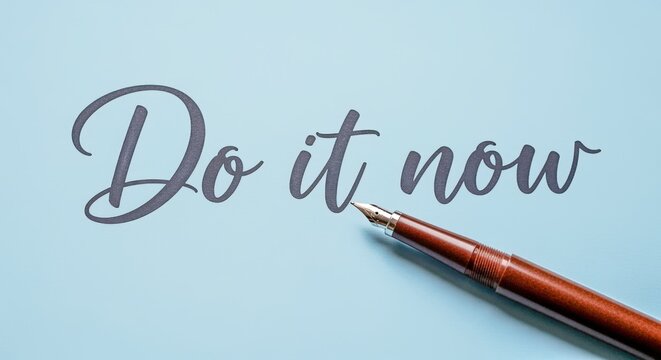 Inspirational message 'Do it now' written in elegant script with a fountain pen on blue paper