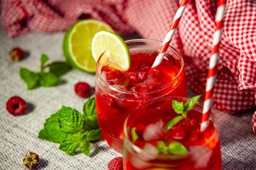 Red drink with lime slices and raspberries floating in ice - macro shot of cooling refreshment.