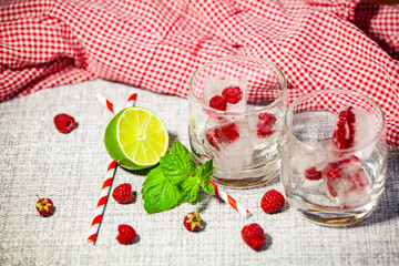 Empty glasses with lime, raspberries and ice. Preparation scene for summer drinks.
