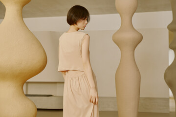 Young woman in beige dress near sculptural forms.