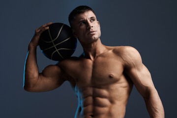 Muscular model sports man with a basketball on dark background. Fashion portrait of strong brutal...