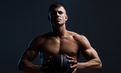 Muscular model sports man with a basketball on dark background. Fashion portrait of strong brutal...