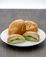 A soft bread filled with creamy pandan custard is displayed on wooden surface, showcasing its smooth texture and vibrant green filling. bread is sliced to reveal rich custard inside
