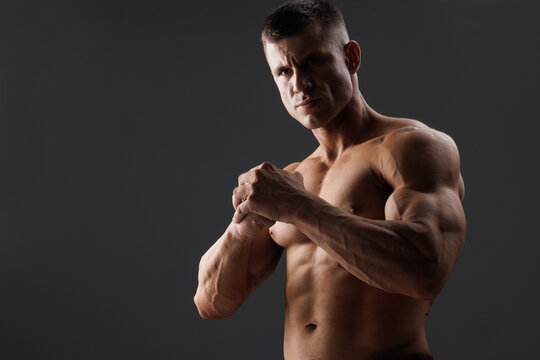 Muscular model sports young man on dark background. Fashion portrait of strong brutal guy. Male flexing his muscles.